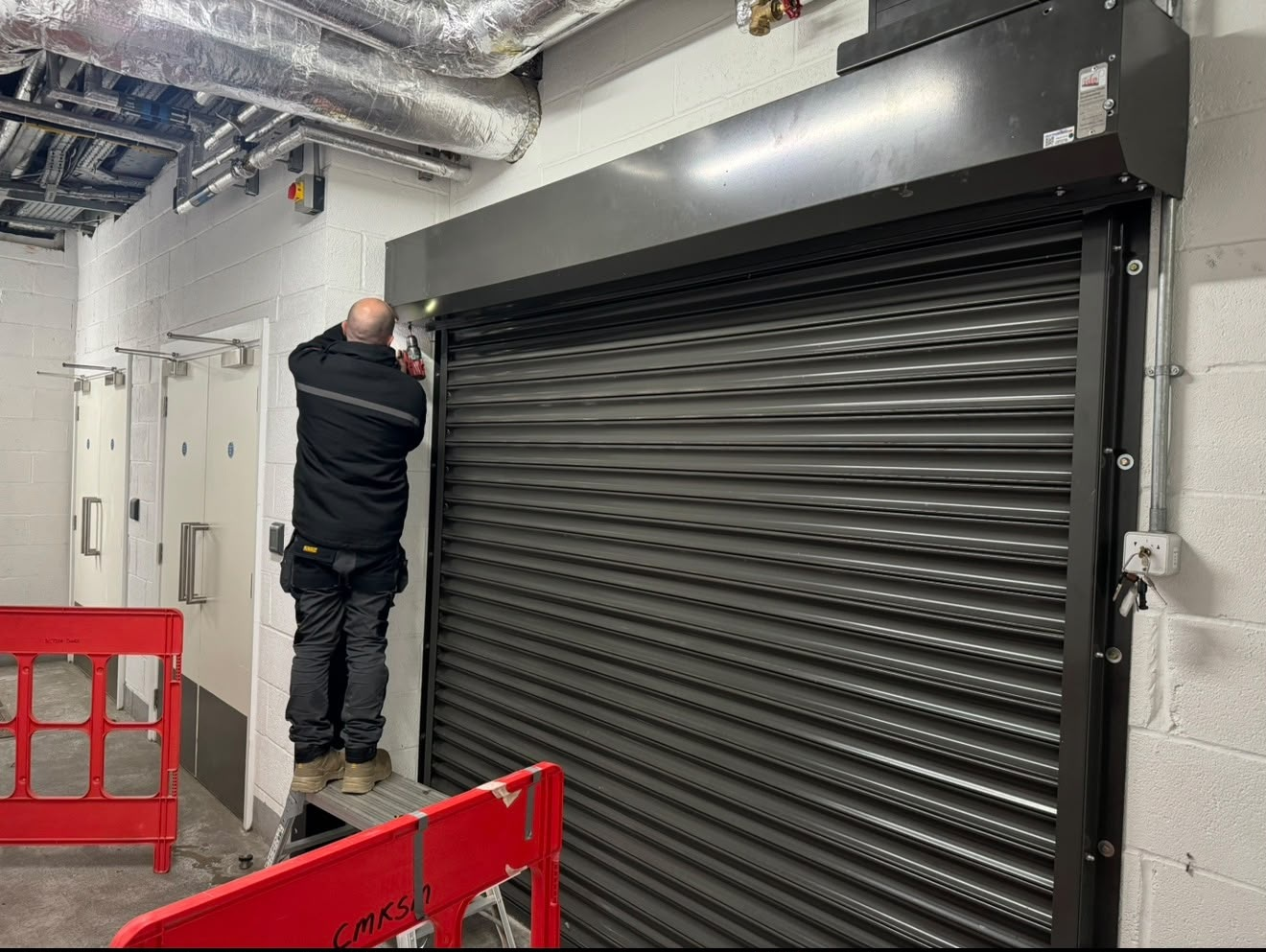 Argents Installations engineer installing a black steel roller shutter inside a commercial building